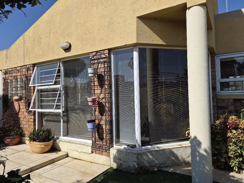 Rear exterior view of the cluster home featuring a brick facade, tiled patio area, and a prominent bay window with top-hung window sections.