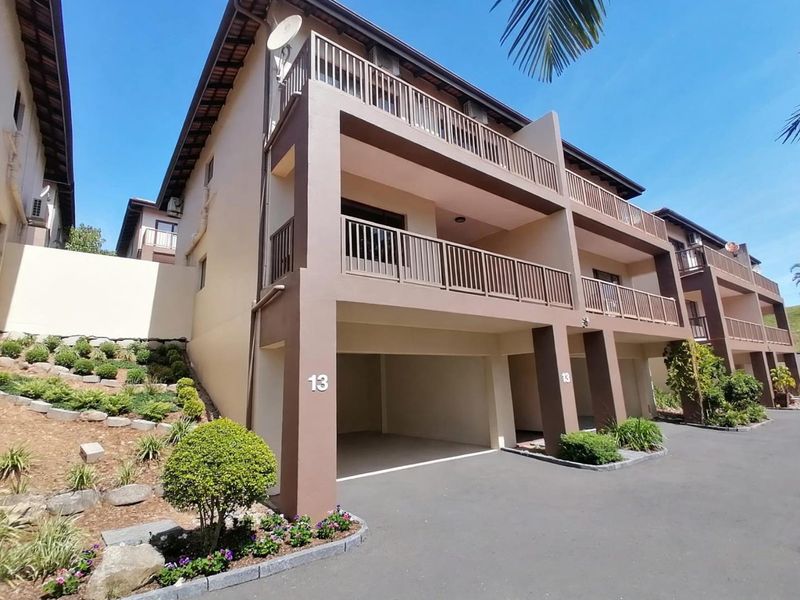 Front elevation of a multi-story townhouse featuring a double garage, private balconies with metal railings, and landscaped garden beds.