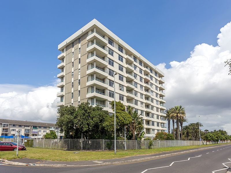 A multi-story apartment building featuring private balconies, set within a landscaped complex with perimeter fencing and street-level access.
