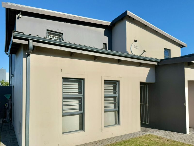 Front elevation of a modern townhouse featuring neutral painted exterior walls, security bars on windows, and a paved entrance walkway.