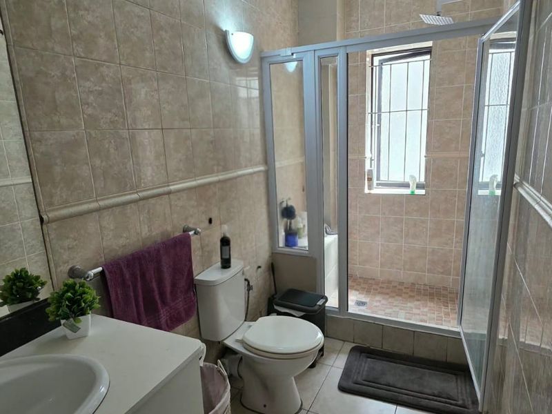 A functional bathroom featuring tiled walls and flooring, a vanity with a basin, a toilet, and a separate shower enclosure with a window.