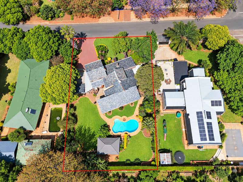 Aerial view of a residential property featuring a swimming pool, landscaped garden, paved driveway, and solar panels on the roof.