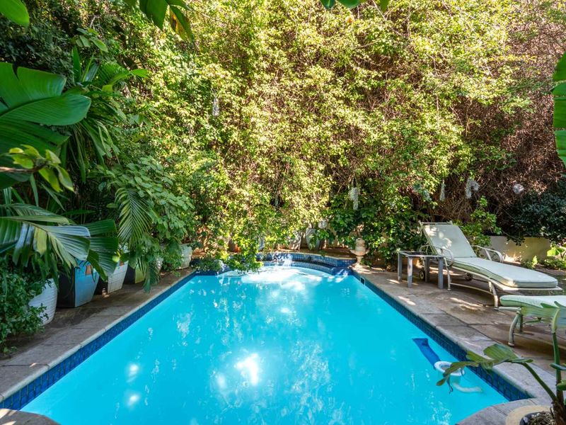 A private swimming pool area surrounded by lush mature greenery and stone paving, offering a secluded outdoor retreat.