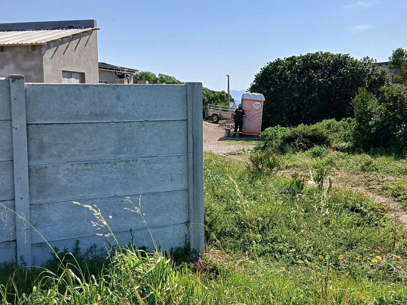 A view of a vacant residential plot featuring a precast concrete boundary wall and natural vegetation.