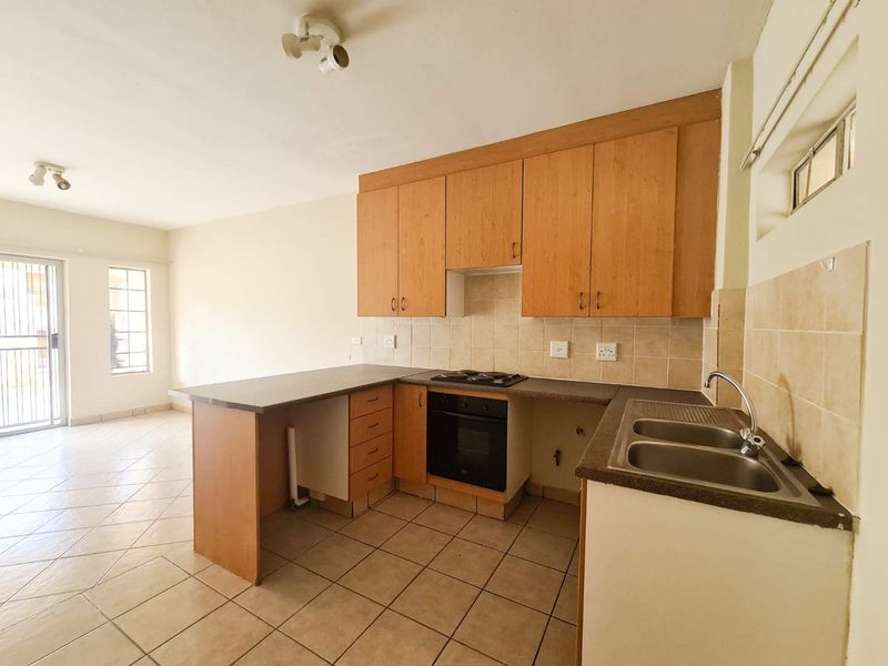 Open plan kitchen featuring wooden cabinetry, built-in oven and hob, tiled flooring, and direct access to an adjacent living area.