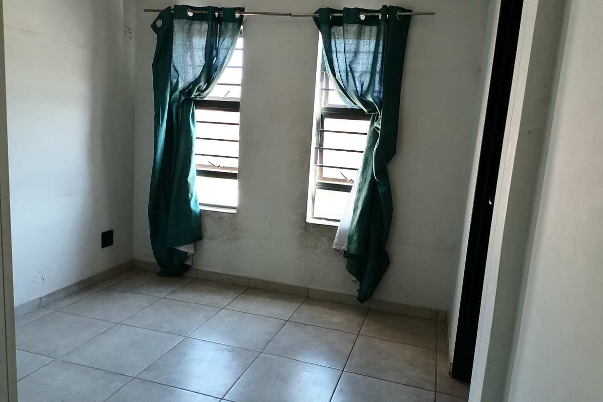 A vacant bedroom featuring tiled flooring and two windows with security bars, requiring minor cosmetic updates to the walls and finishes.
