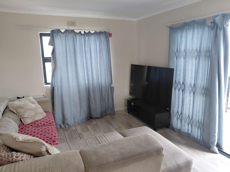 A living room featuring tiled flooring, a window, and a sliding door with a security gate providing access to the exterior.