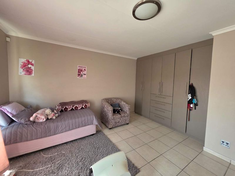 A well-maintained bedroom featuring neutral wall tones, practical built-in cupboards, and durable tiled flooring, offering a clean and functional living space.