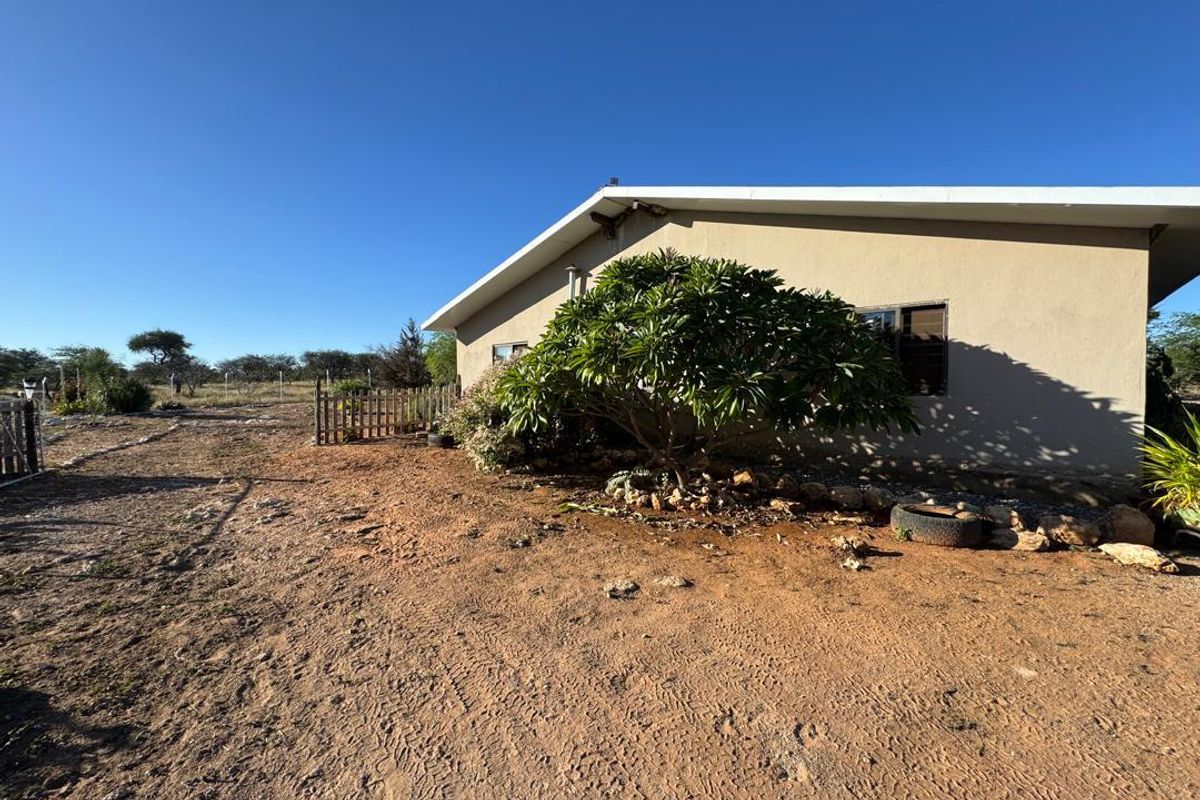 A view of the rear exterior of the property, featuring a simple building structure set against a natural, unpaved landscape.