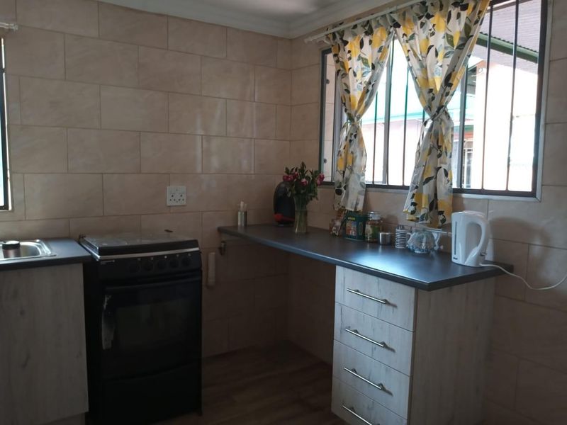 A functional kitchen featuring light wood-finish cabinetry, dark laminate countertops, a tiled splashback, and a freestanding stove with a stainless steel sink.