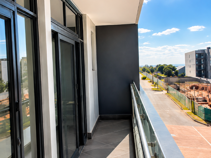 A modern, clean balcony featuring tiled flooring, a sleek glass balustrade, and large sliding glass doors providing access to the interior.