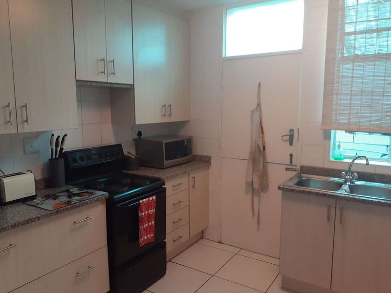A functional kitchen featuring light-toned cabinetry, granite-look laminate countertops, a double bowl sink, and tiled flooring with a practical layout.