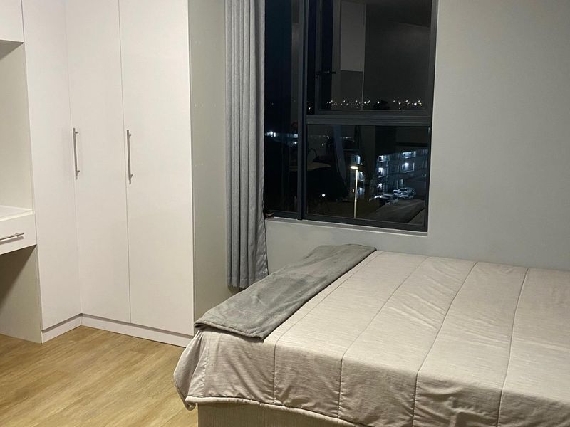 A modern bedroom featuring built-in cupboards, a integrated vanity unit, and laminate flooring, with a large window providing natural light.
