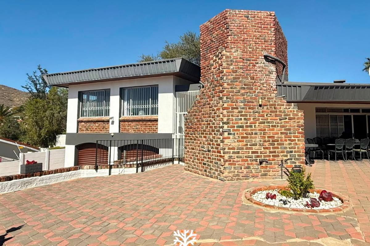 Rear exterior view featuring a prominent brick chimney, paved patio area, and secure building facade with metal security bars.