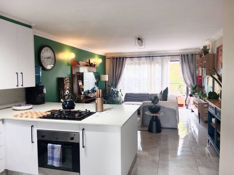Open-plan living area featuring a modern kitchen with a central island, gas hob, built-in oven, and seamless flow to a bright balcony.