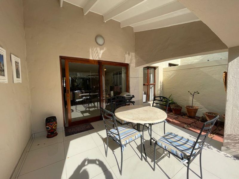 A covered patio area featuring tiled flooring, exposed beam ceiling, and sliding glass door access to the interior living space.