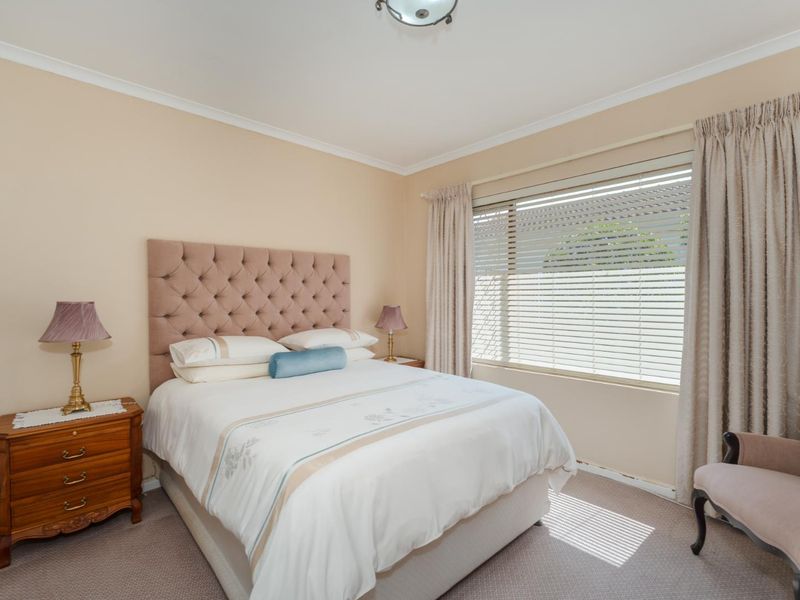 A well-maintained bedroom featuring neutral wall tones, carpeted flooring, and a large window with venetian blinds for natural light.