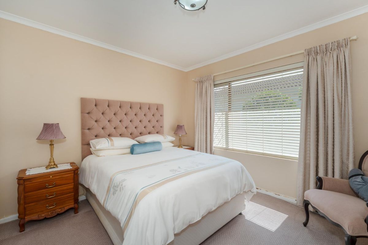 A well-maintained bedroom featuring neutral wall tones, carpeted flooring, and a large window with venetian blinds for natural light.