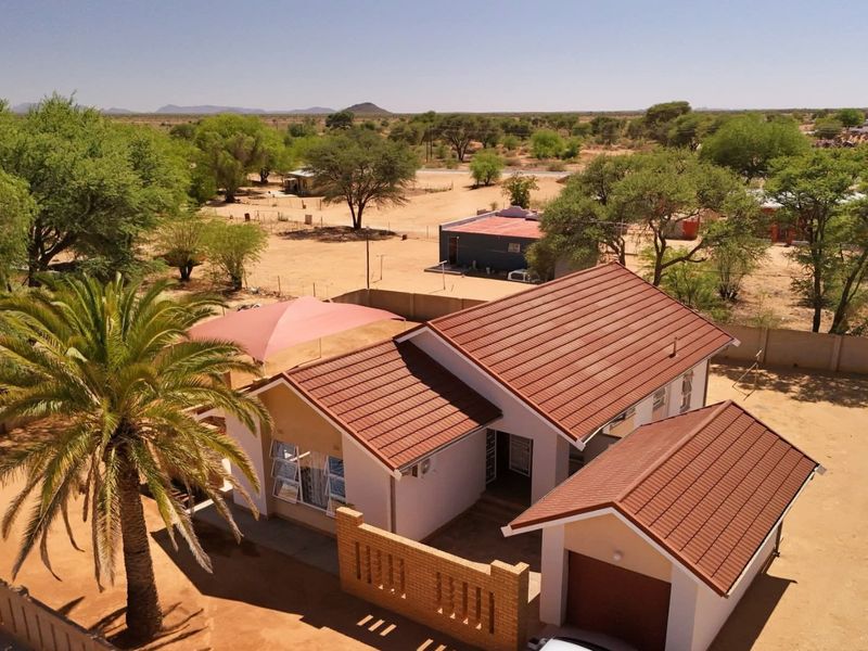 Aerial view of a residential property featuring a tiled roof house, attached garage, brick boundary wall, and a shaded outdoor area.