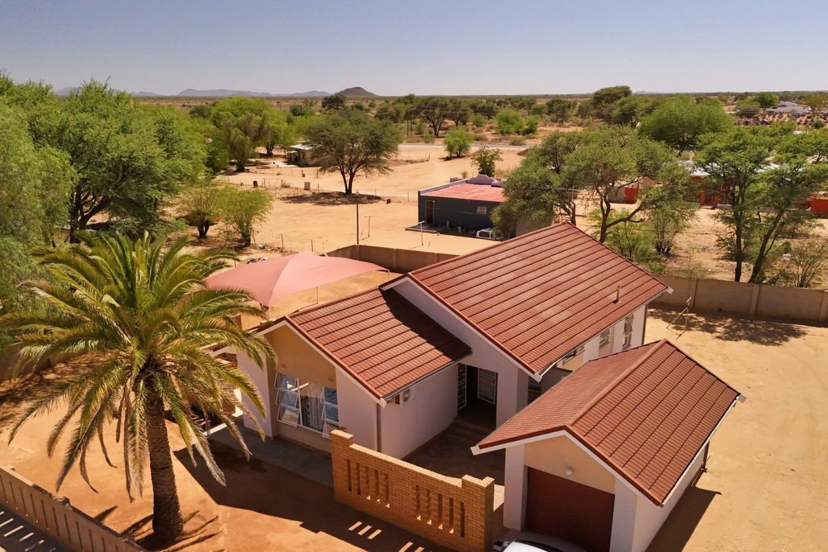 Aerial view of a residential property featuring a tiled roof house, attached garage, brick boundary wall, and a shaded outdoor area.