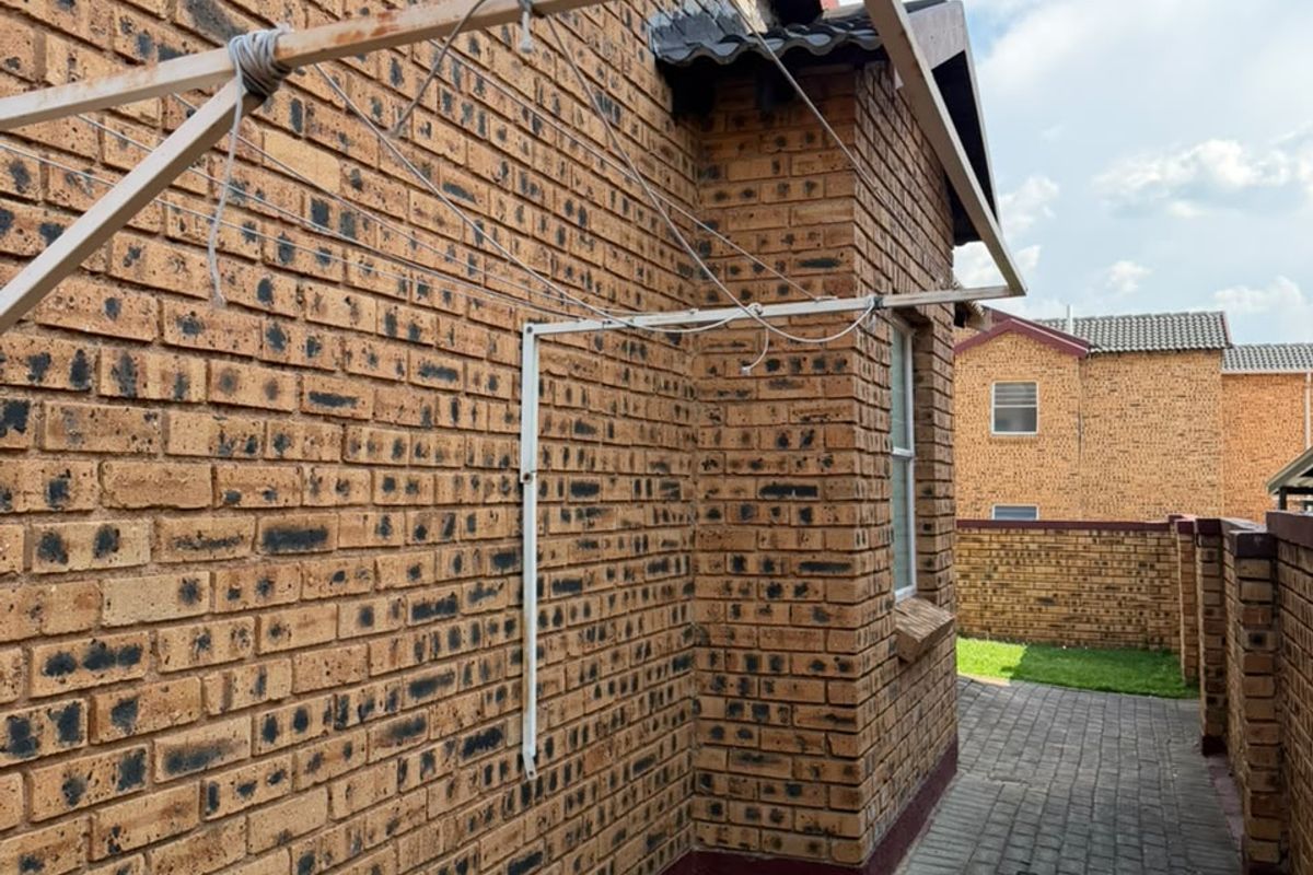 A side exterior view of the property featuring face brick walls, a paved walkway, and a wall-mounted washing line.