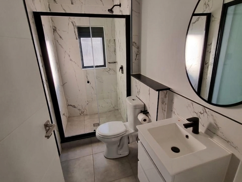Modern bathroom featuring a walk-in shower with black-framed glass, marble-look wall tiles, a sleek wall-mounted vanity, and contemporary black fixtures.