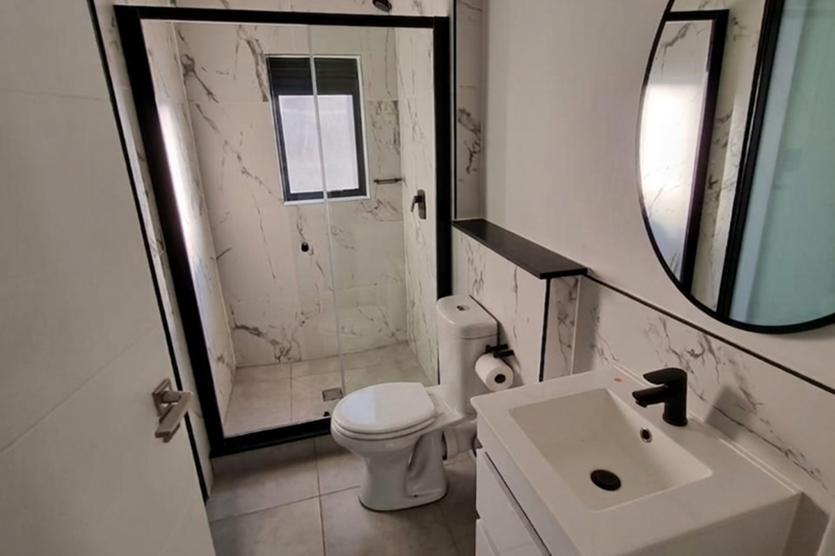 Modern bathroom featuring a walk-in shower with black-framed glass, marble-look wall tiles, a sleek wall-mounted vanity, and contemporary black fixtures.