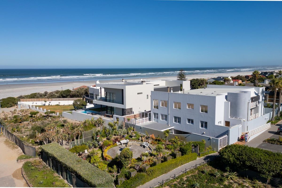 Aerial view of a modern beachfront apartment complex featuring landscaped gardens, a swimming pool, and direct access to the coastline.