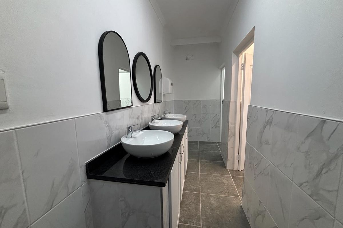 A clean, modern office bathroom featuring a triple vanity with vessel sinks, stone countertops, and marble-look wall tiling.