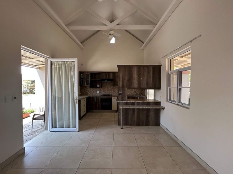 Spacious open-plan living area featuring a vaulted ceiling, tiled floors, and a modern kitchen with granite countertops and built-in appliances, opening to a patio.