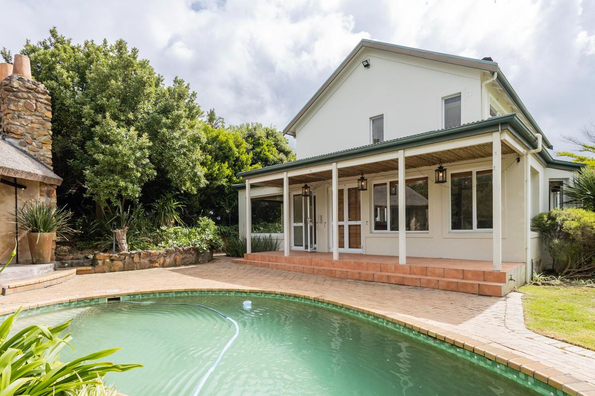 Rear view of the property featuring a swimming pool, paved patio area, covered veranda, and a distinctive stone chimney.