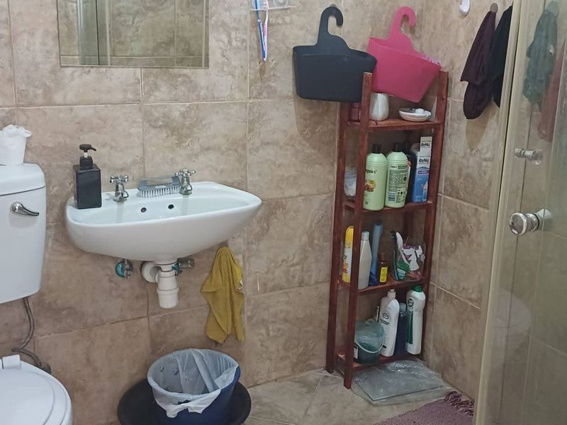 A functional bathroom featuring tiled walls and flooring, a wall-mounted basin, a standard toilet, and a glass-enclosed shower unit.