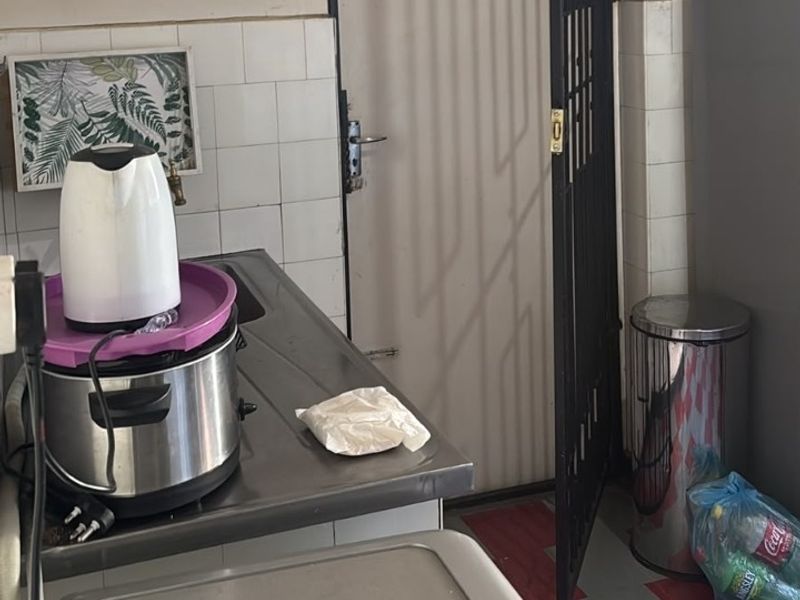 A compact kitchen area featuring a stainless steel sink, tiled splashback, and a security gate leading to an exterior space.