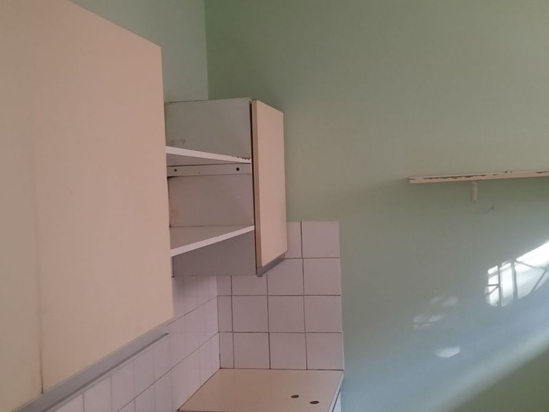 A compact kitchen area featuring built-in cabinetry, tiled splashbacks, and wall-mounted shelving, offering a blank canvas for potential renovation and modernization.