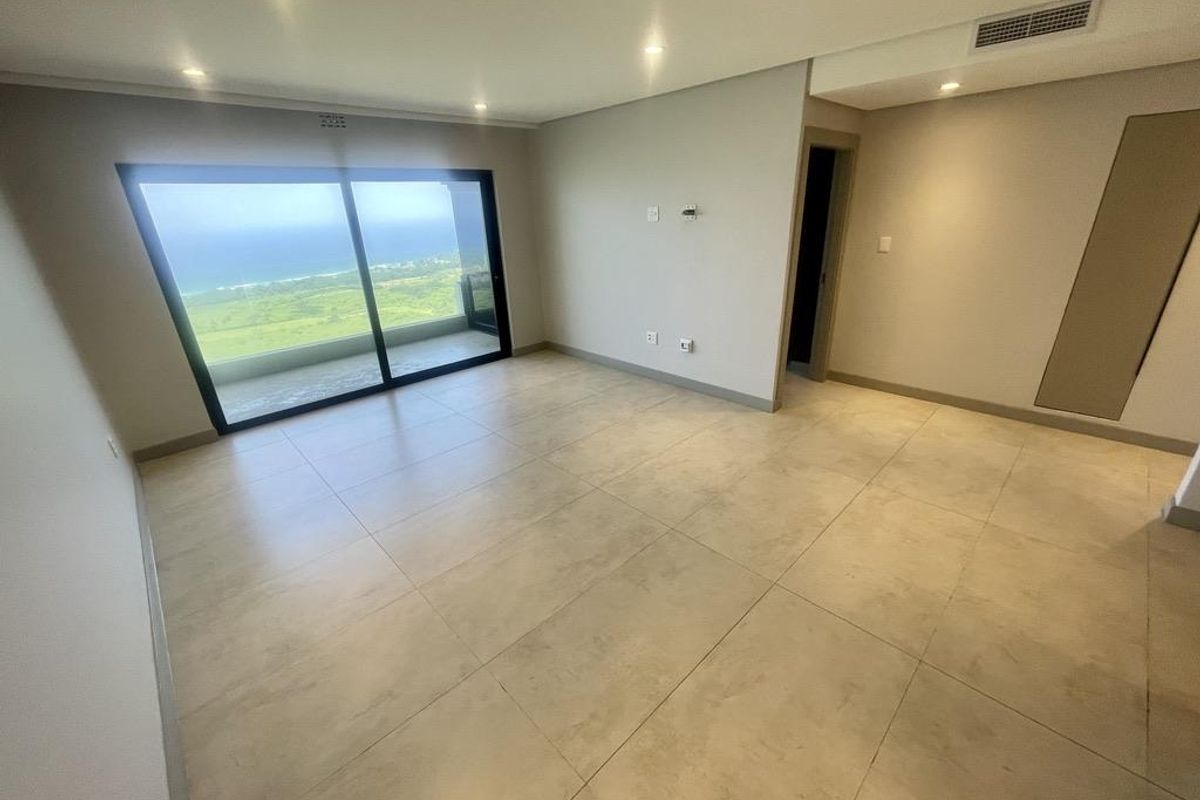 Spacious, modern living area featuring large sliding glass doors that open to a balcony with scenic coastal views and integrated ceiling lighting.