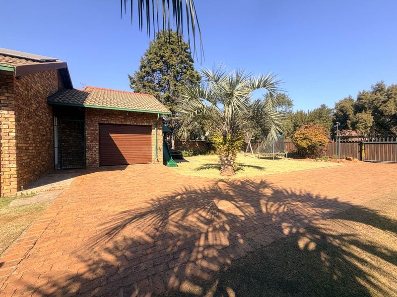 A spacious rear exterior area featuring brick paving, a single garage, and a well-maintained garden with established landscaping and perimeter fencing.
