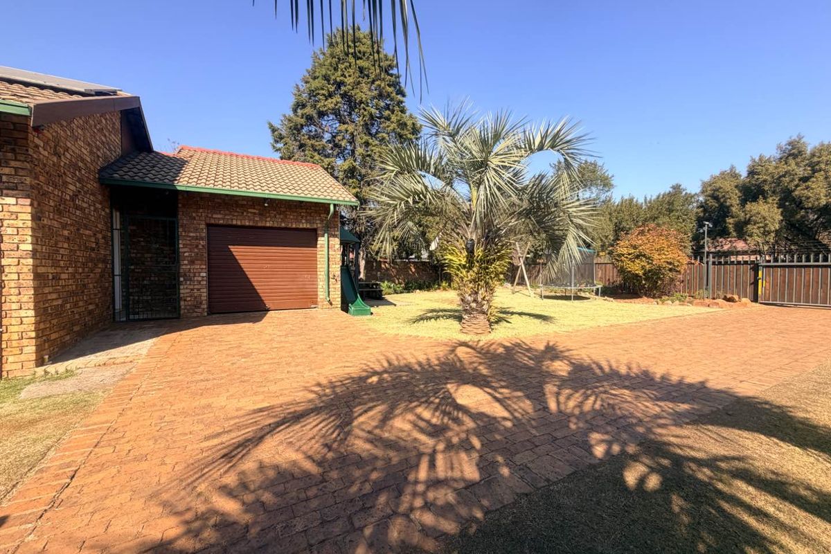 A spacious rear exterior area featuring brick paving, a single garage, and a well-maintained garden with established landscaping and perimeter fencing.