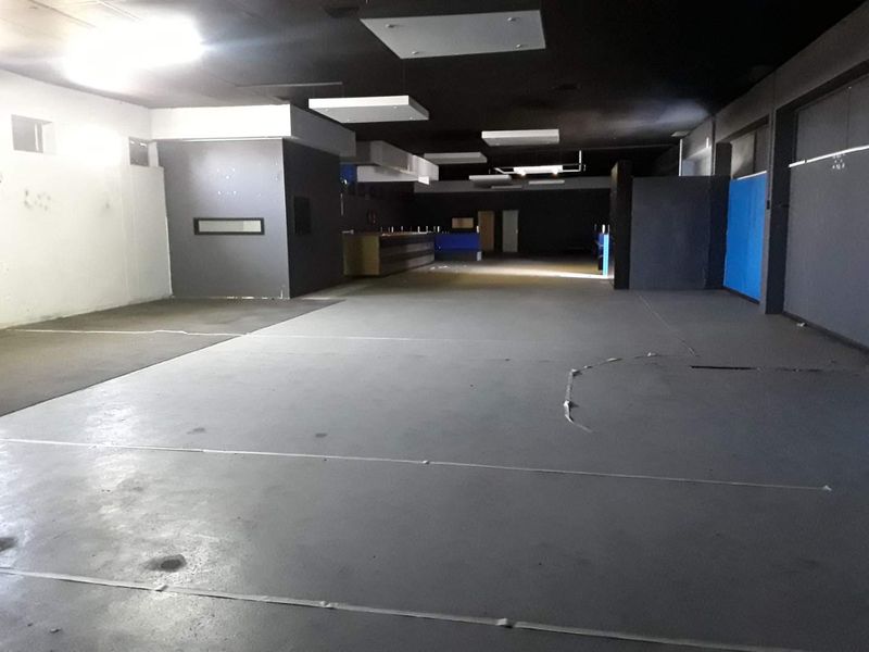 A large, open-plan commercial space featuring dark painted ceilings, recessed lighting, and concrete flooring, suitable for various business or retail applications.
