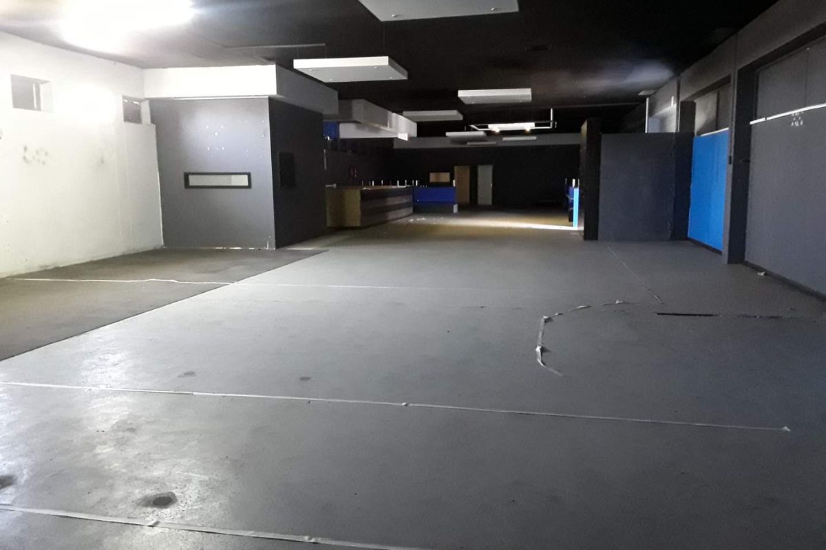 A large, open-plan commercial space featuring dark painted ceilings, recessed lighting, and concrete flooring, suitable for various business or retail applications.