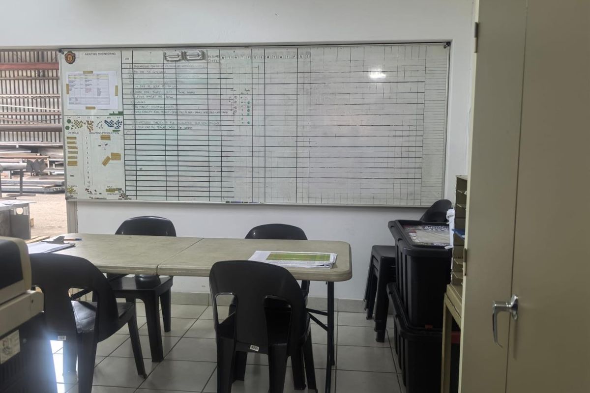 A functional utility or office space featuring tiled flooring, a large wall-mounted whiteboard, and a metal storage cabinet.