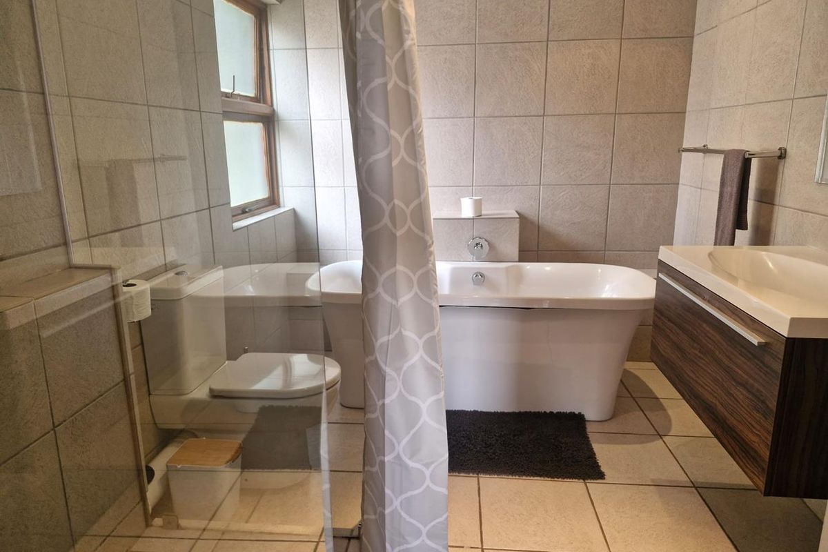 A well-appointed bathroom featuring a freestanding bathtub, a glass-enclosed shower, a modern wall-mounted vanity, and neutral floor-to-ceiling tiling.