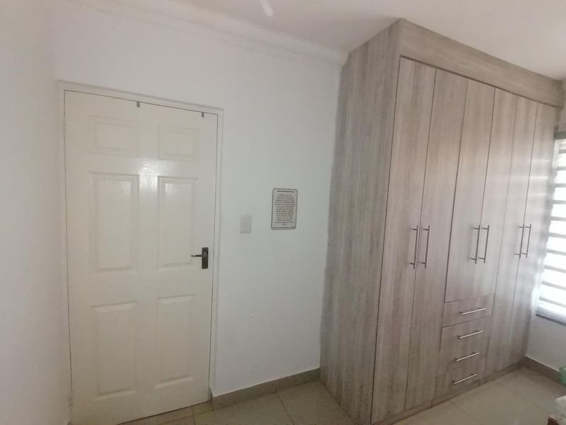 A clean, empty bedroom featuring neutral tiled flooring and modern light-wood built-in cupboards with ample storage space.