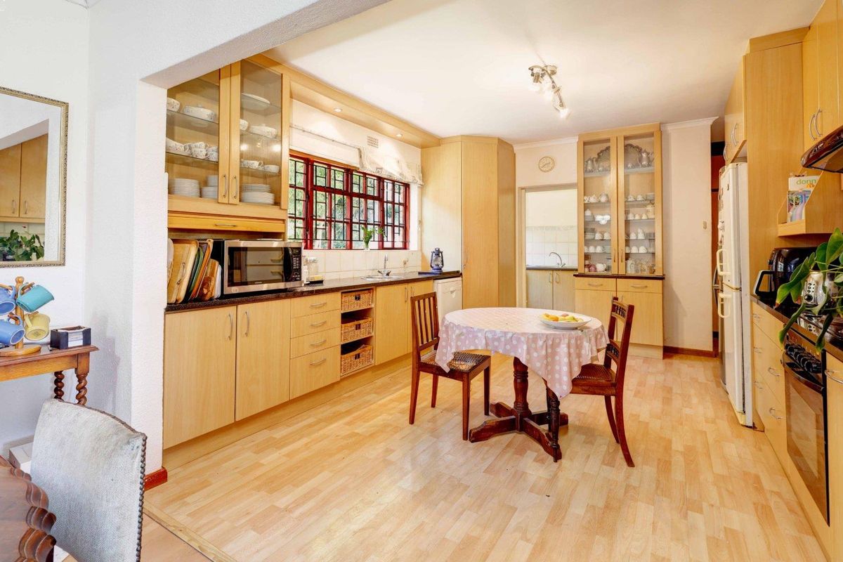 A functional kitchen featuring light wood cabinetry, glass-fronted display units, laminate flooring, and a dedicated dining area with ample storage space.