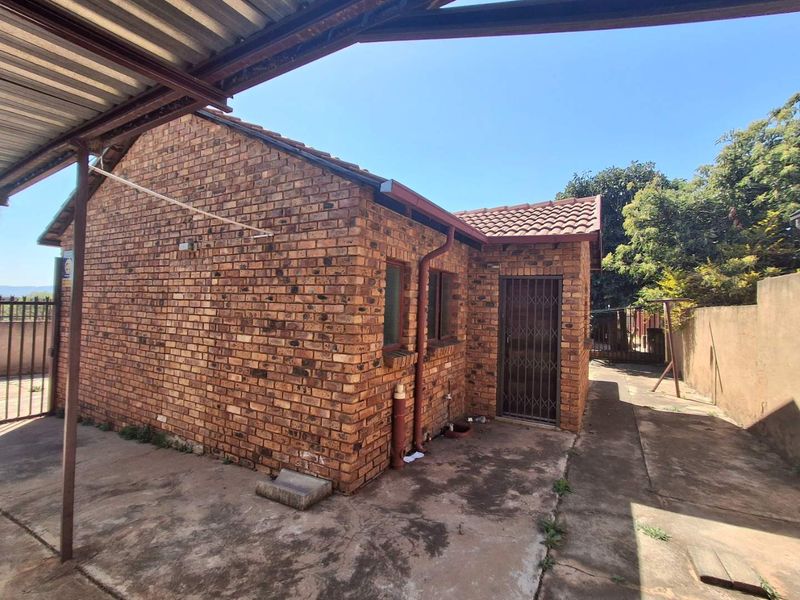 Rear view of the property featuring face brick construction, a tiled roof, and a covered concrete patio area with security gate access.