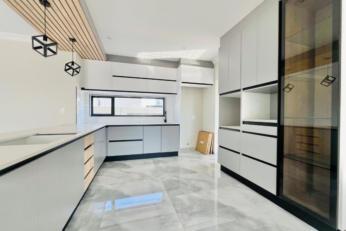 Modern kitchen featuring sleek handleless cabinetry, stone countertops, marble-look floor tiles, and a stylish slatted timber ceiling detail with pendant lighting.