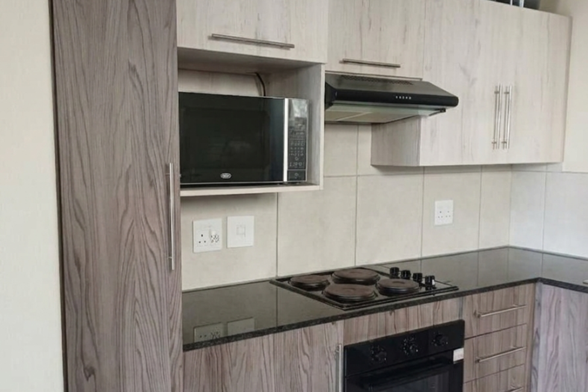 Modern kitchen featuring wood-grain cabinetry, granite countertops, integrated oven, hob, and extractor fan with neutral tiled backsplash and flooring.