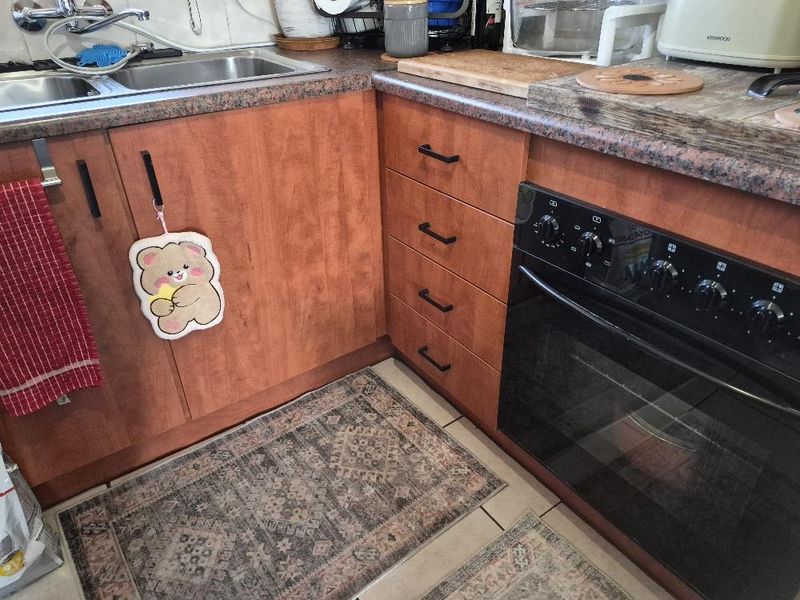 A functional kitchen area featuring wood-tone cabinetry, a built-in oven, laminate countertops, and a stainless steel double sink with tiled flooring.