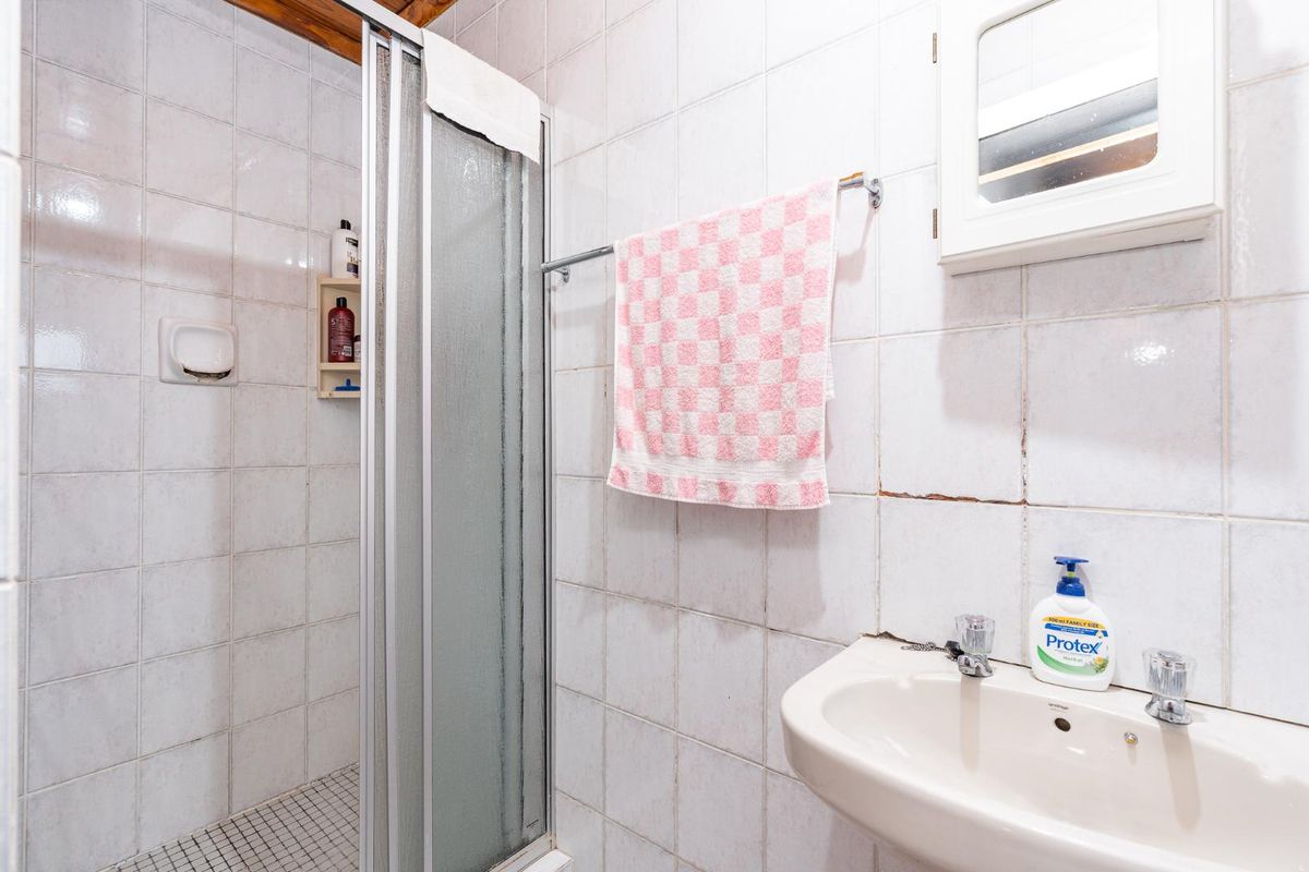 A functional bathroom featuring a shower enclosure, wall-mounted basin, and tiled finishes, currently showing signs of wear and requiring maintenance.