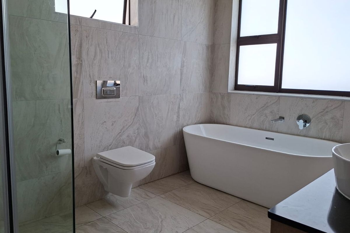 Modern bathroom featuring a wall-mounted toilet, a freestanding bathtub, a glass-enclosed shower, and contemporary floor-to-ceiling tiling.