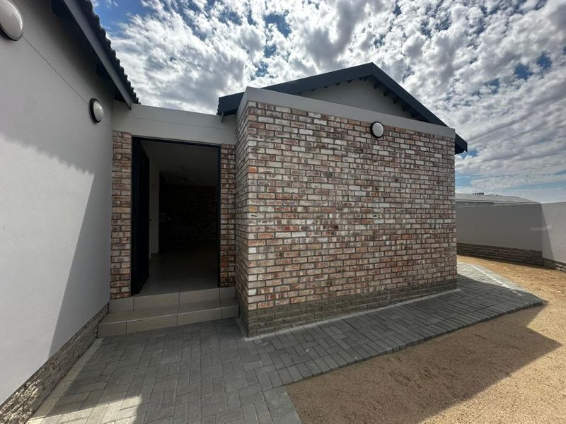 A modern rear exterior view featuring a clean exposed brick facade, paved walkway, and a tiled entrance step leading into the home.